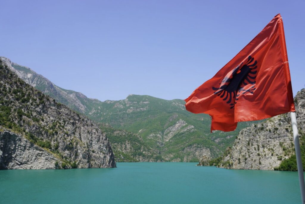 Uitzicht over Koman Meer en omliggende bergen met vlag van Albanië vanaf veerboot