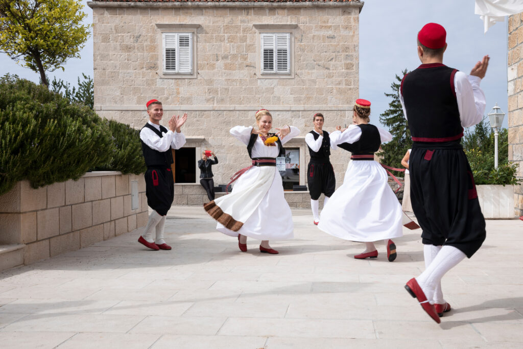 Mannen en vrouwen dragen traditionele Kroatische kleding terwijl ze dansen en een show opvoeren in een landelijke omgeving met een typisch Dalmatische omgeving in Dalmatië