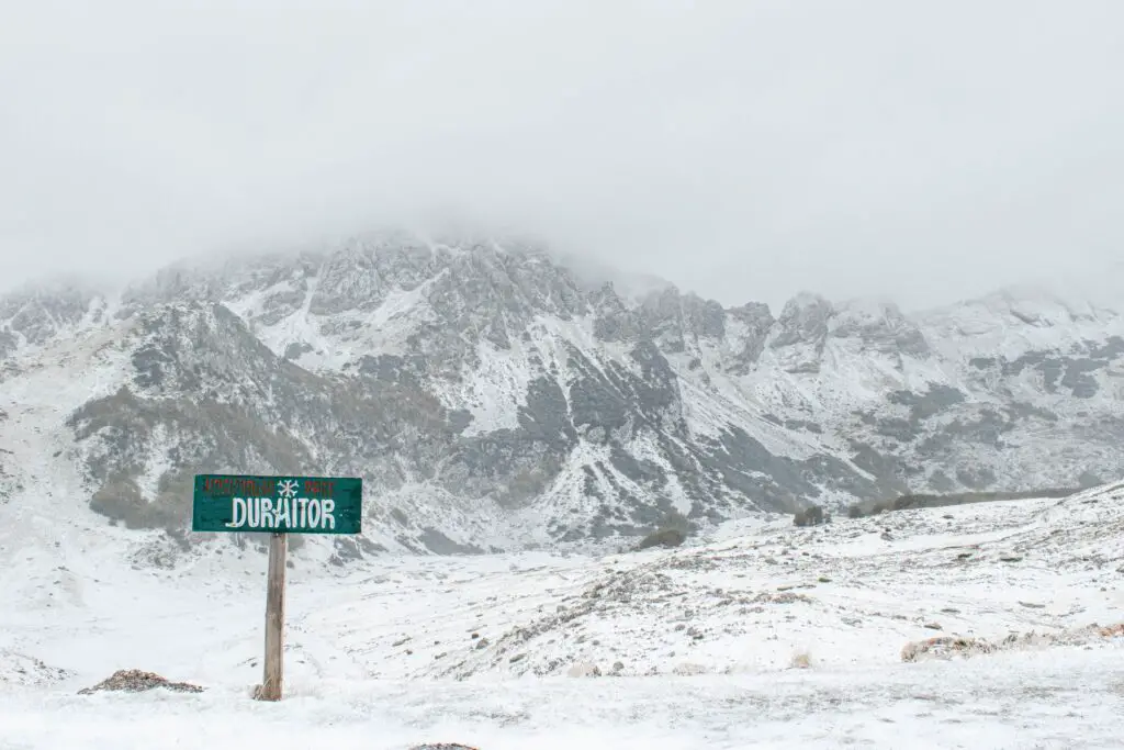 Een groen bord met Nationaal Park Durmitor langs een besneeuwde berg in Montenegro in de winter